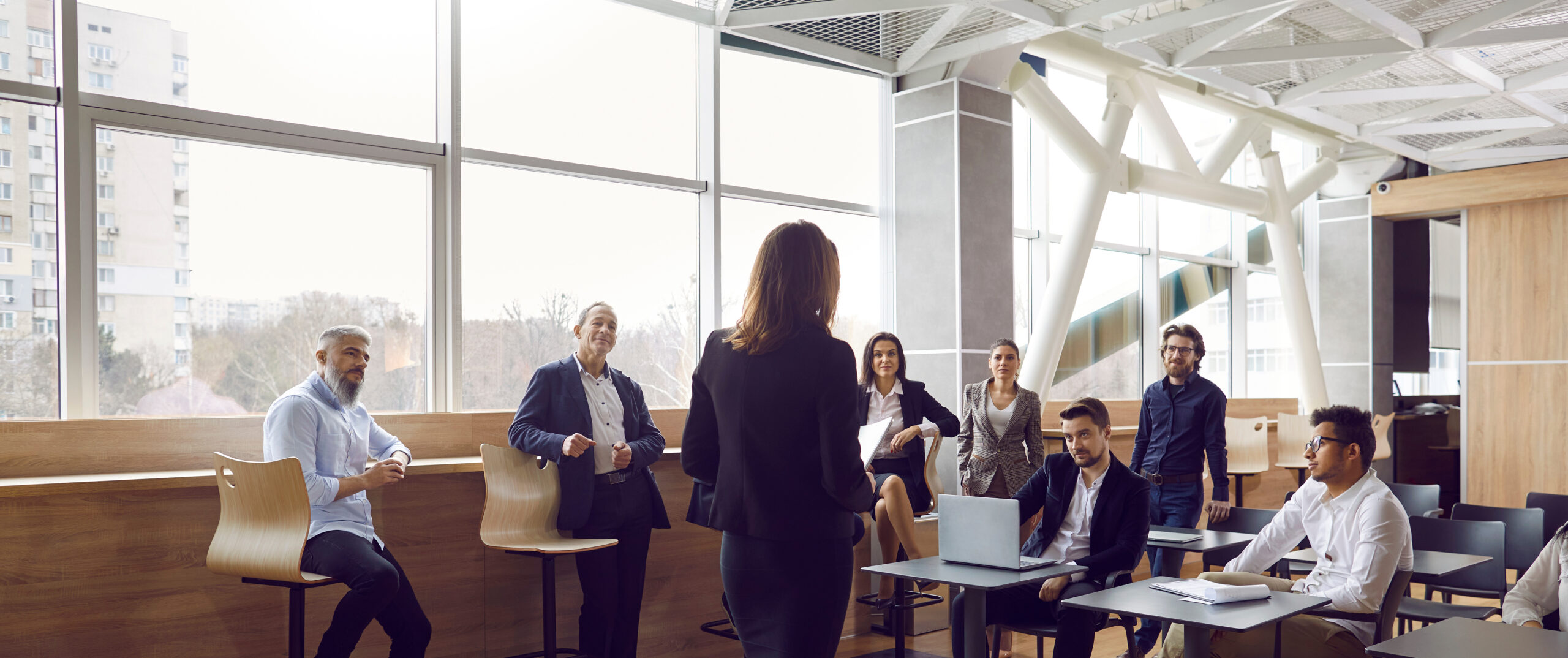 Various businessmen listen to female business leader during corporate meeting or training lecture.